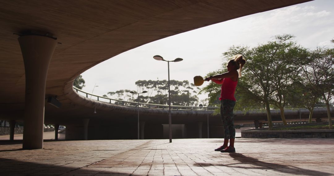 Woman exercising with kettlebell outdoors under highway - Free Images, Stock Photos and Pictures on Pikwizard.com