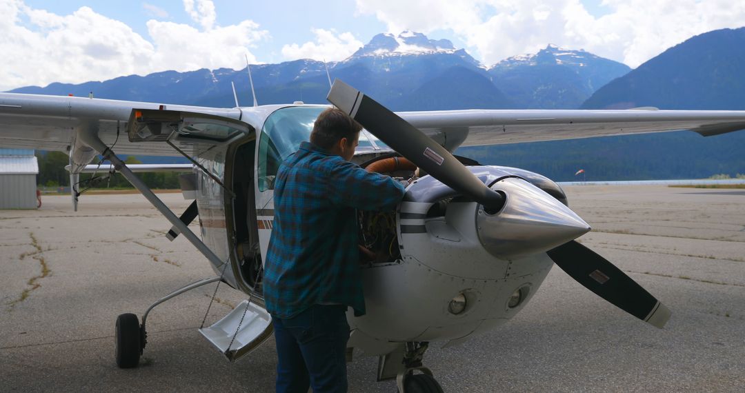 Man Inspecting Small Aircraft with Mountain Background on Tarmac - Free Images, Stock Photos and Pictures on Pikwizard.com