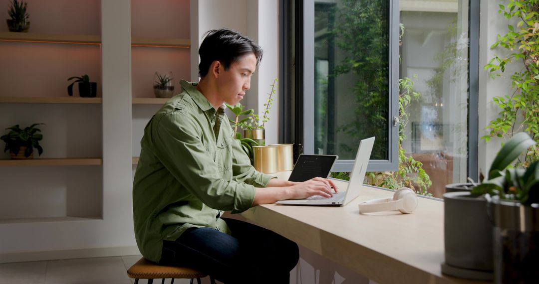 Man Working on Laptop at Modern Home Workspace by Window