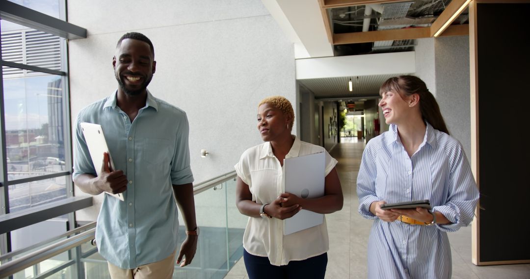 Diverse Colleagues Walking in Office Hallway Holding Documents and Gadgets