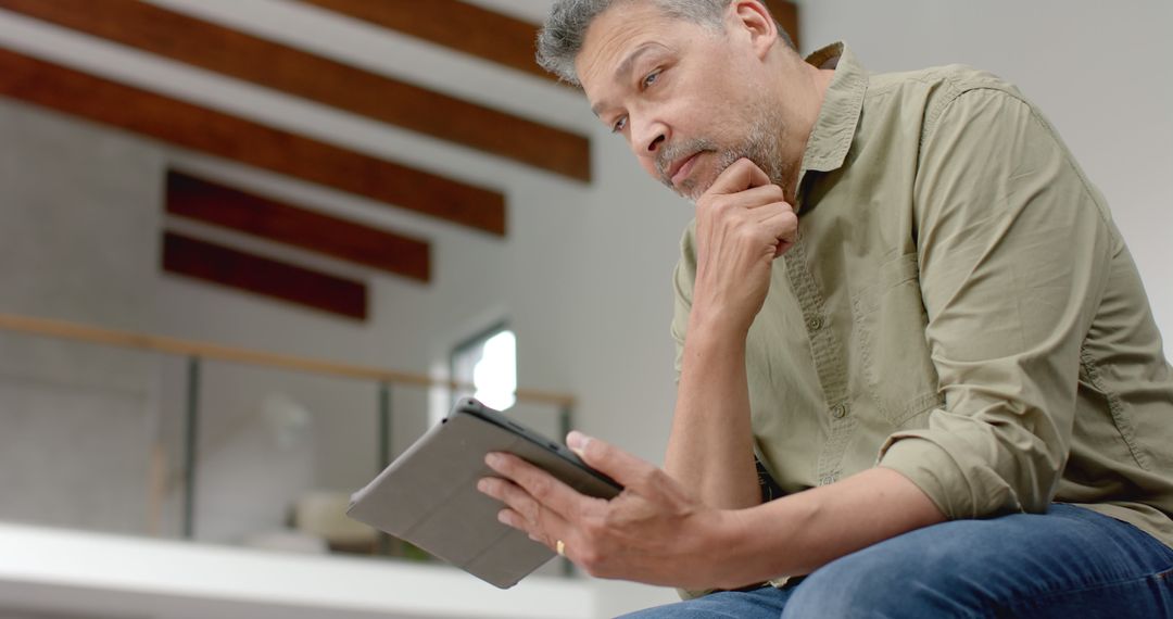 Man Contemplating Options While Using Tablet in Modern Home - Free Images, Stock Photos and Pictures on Pikwizard.com