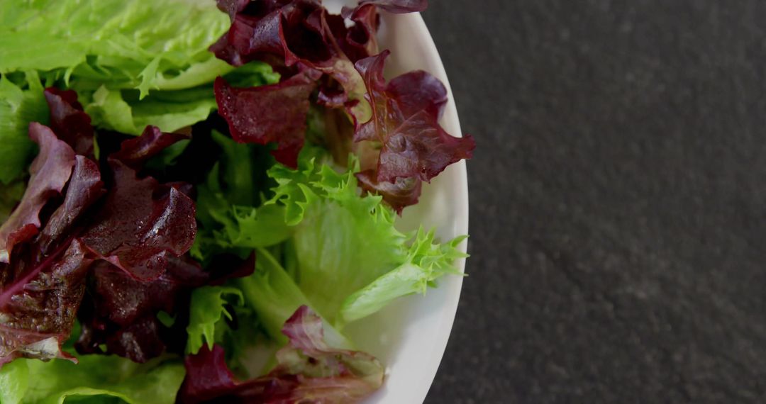 Mixed Green and Red Leaf Lettuce in White Bowl on Dark Countertop