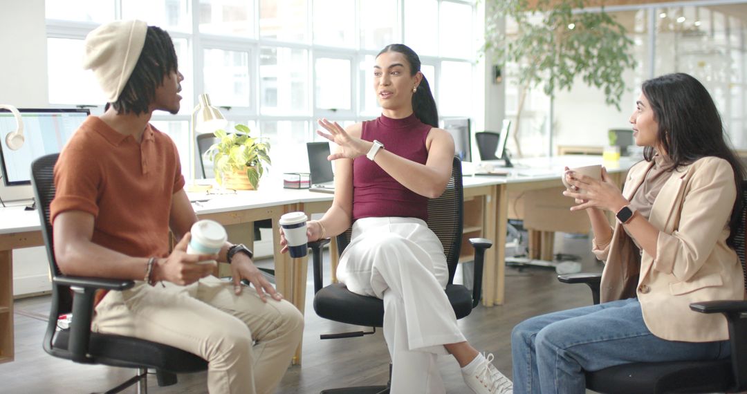 Diverse coworkers collaborating and sharing ideas over coffee in sunlit open-plan office