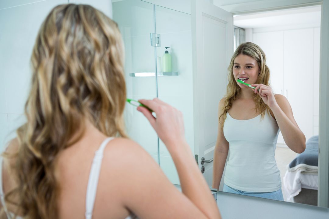 Woman looking in mirror while brushing her teeth in bathroom - Free Images, Stock Photos and Pictures on Pikwizard.com