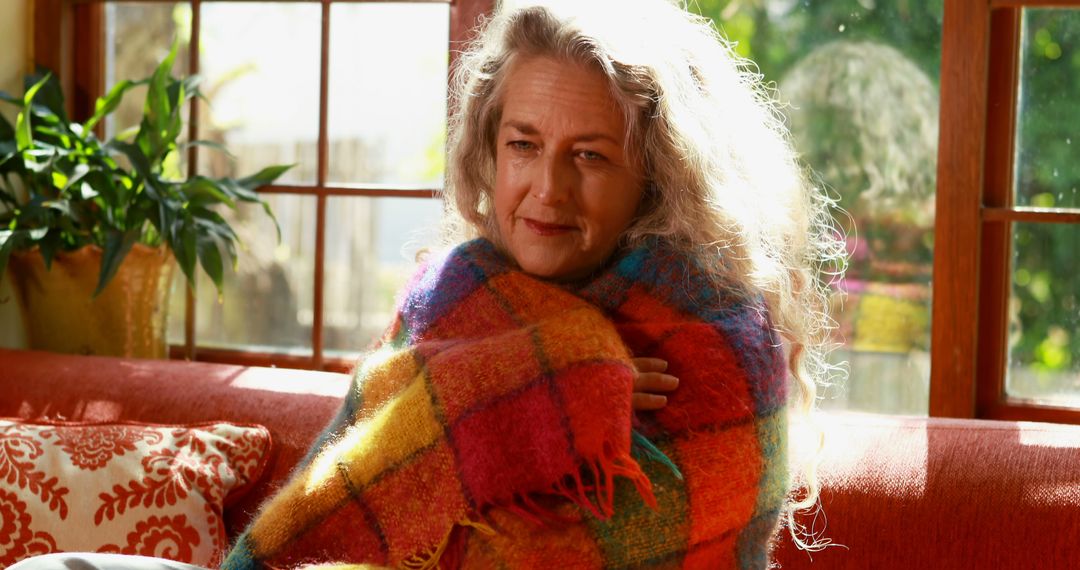 Caucasian woman wrapped in a colorful blanket at home - Free Images, Stock Photos and Pictures on Pikwizard.com