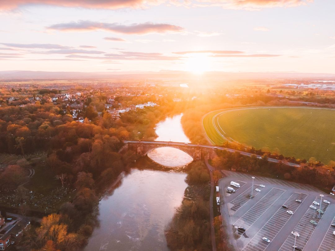 River reflecting golden sunset over arched bridge with glowing fields and parking lot