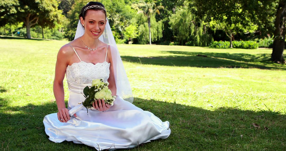 Smiling Bride Sitting on Grass Holding Bouquet in Green Park - Free Images, Stock Photos and Pictures on Pikwizard.com