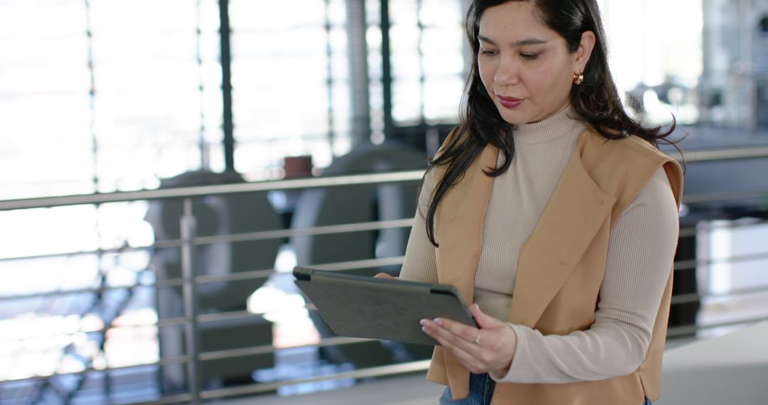 Young professional woman using tablet in modern office lobby with mezzanine and railing