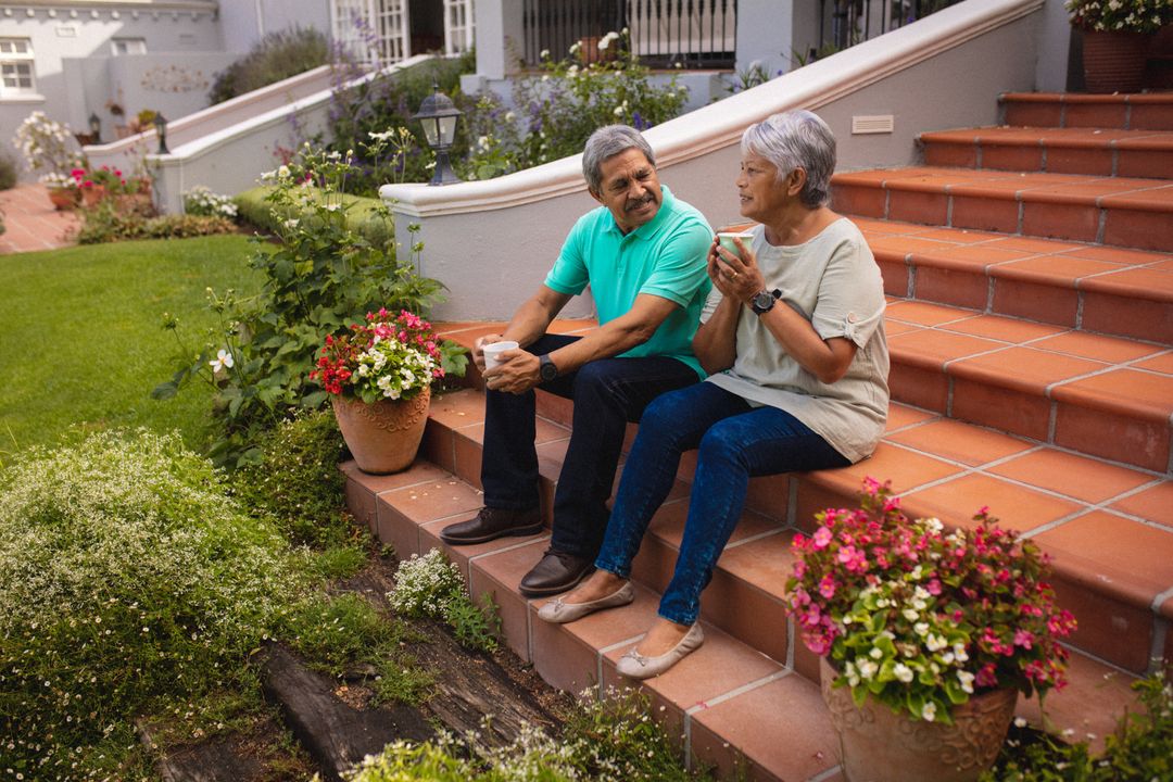 Biracial senior couple with coffee cups talking while sitting on staircase against house in yard - Free Images, Stock Photos and Pictures on Pikwizard.com