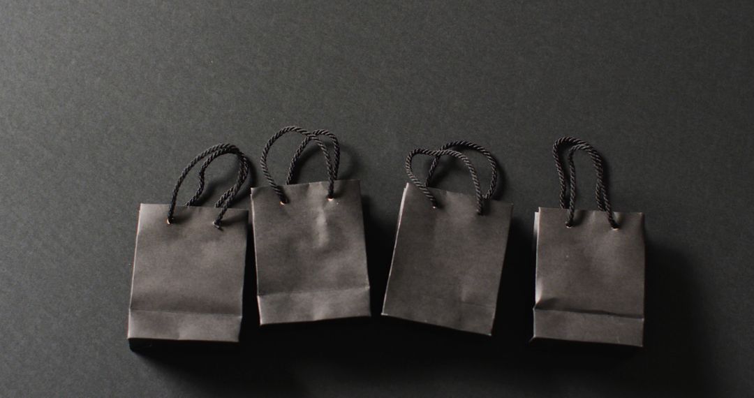 Four black gift bags with black handles in a row on dark grey background with copy space - Free Images, Stock Photos and Pictures on Pikwizard.com