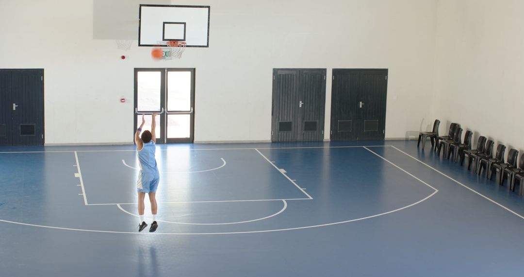 Man Practicing Basketball Indoors on Blue Court