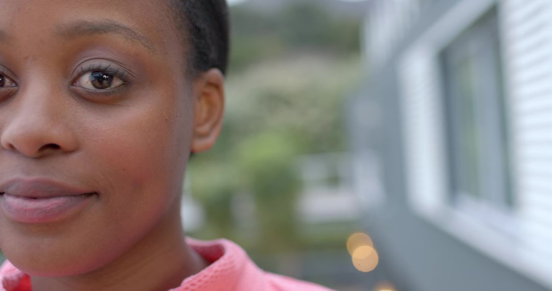 African American woman gazing on balcony wearing pink collared top with soft bokeh urban