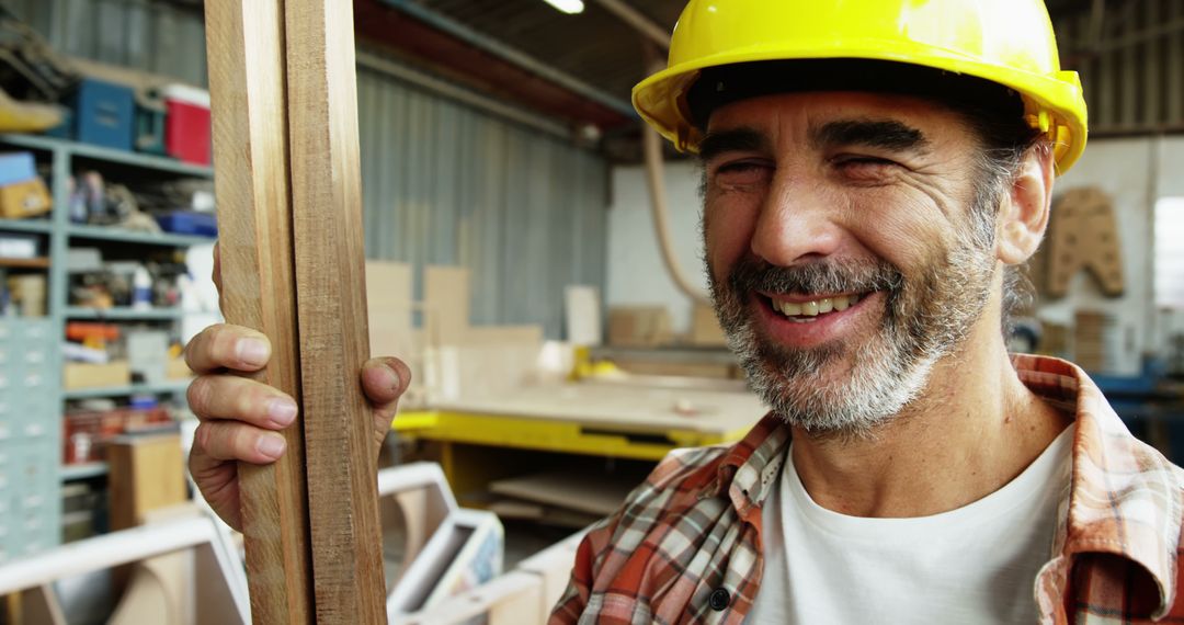 Happy Carpenter Holding Wooden Planks in Workshop with Hard Hat - Free Images, Stock Photos and Pictures on Pikwizard.com