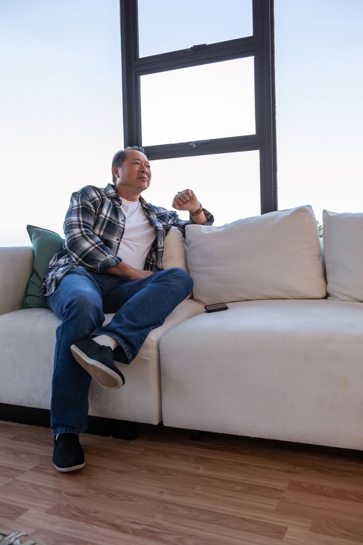 Man Relaxing on Couch by Window with Smartphone in Casual Setting