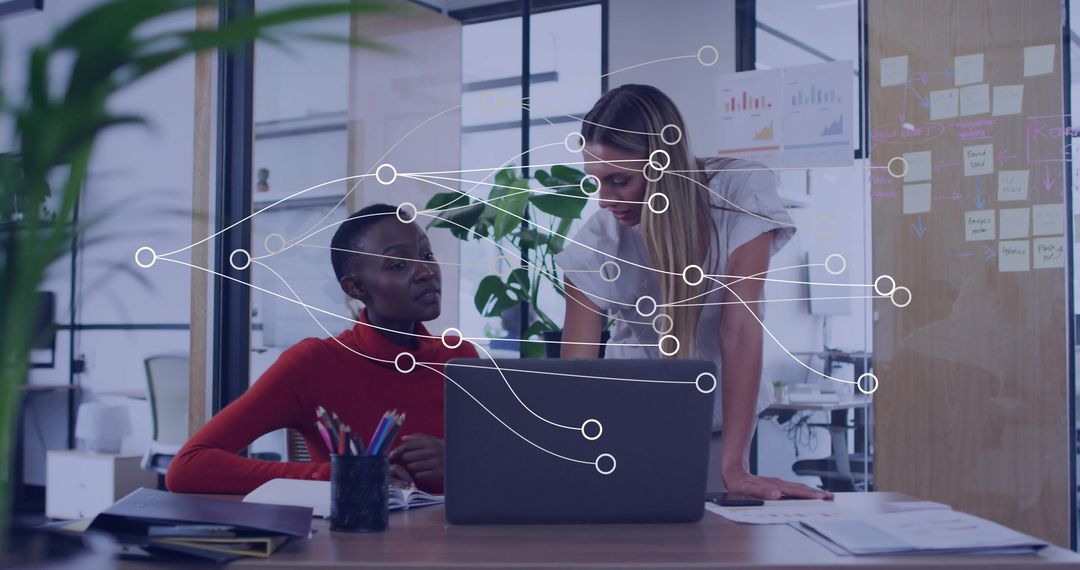 Two women collaborating over laptop in modern office with data visualization overlay