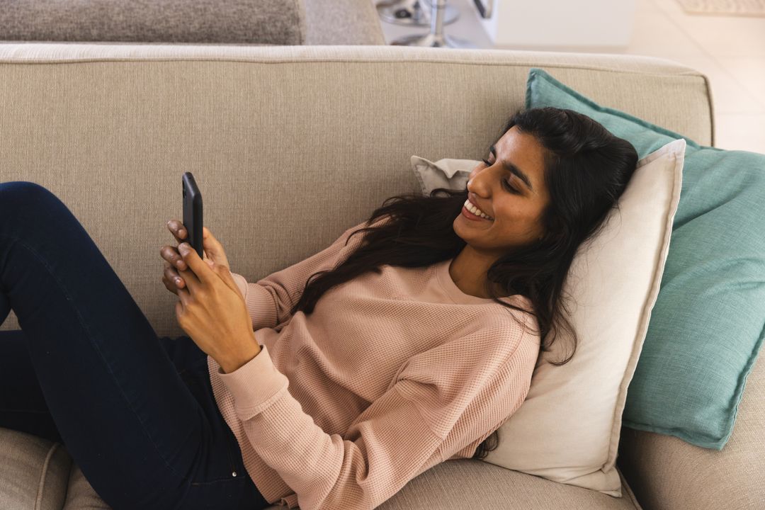Smiling Woman Relaxing on Sofa While Engaging with Smartphone
