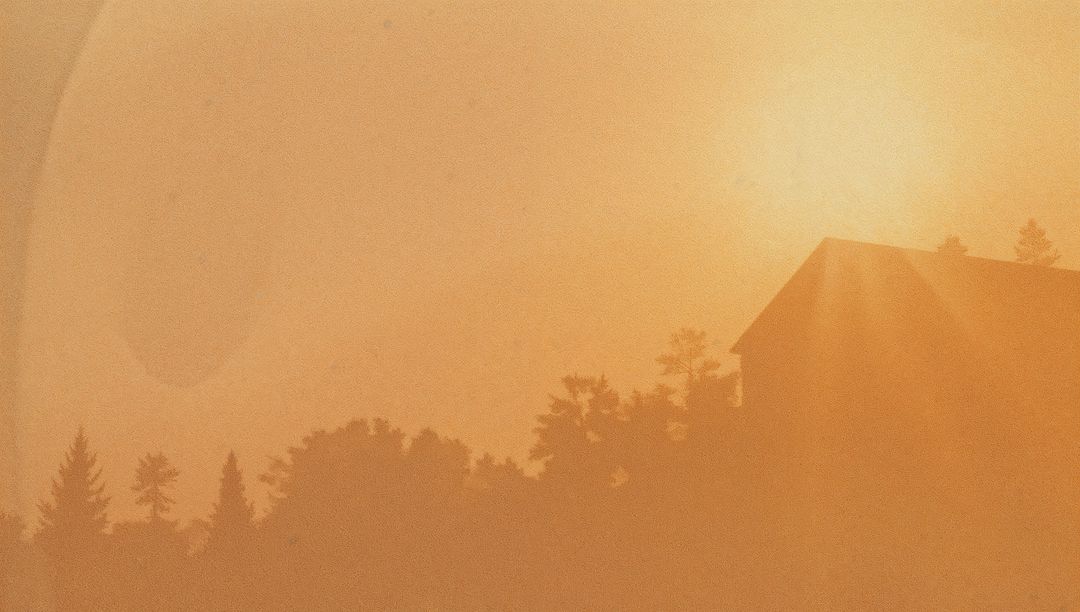Glowing sun casting golden rays over silhouetted house and conifer treeline at hazy dusk