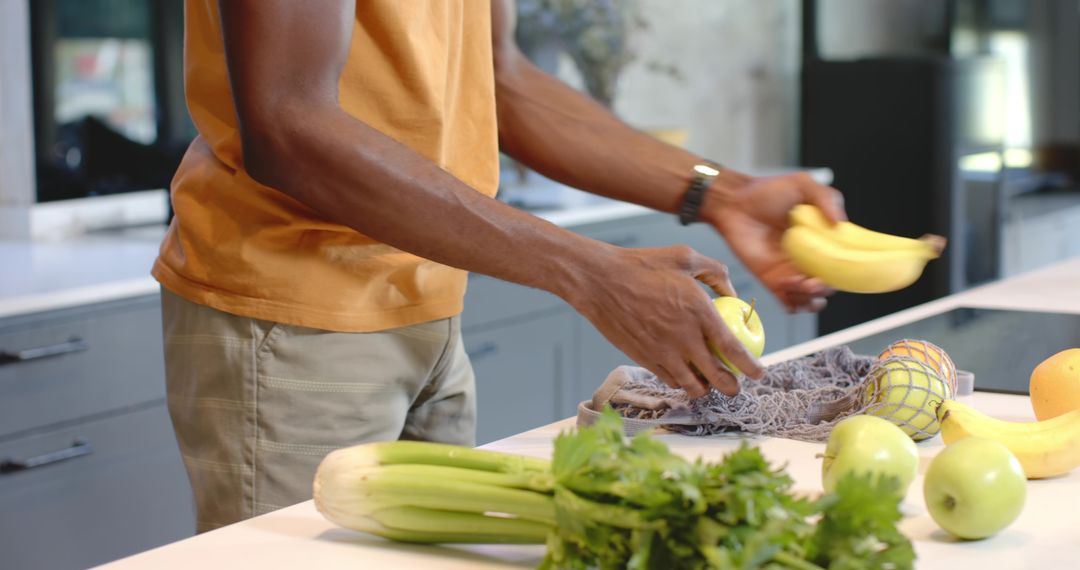 African American man arranging fresh bananas and green apples on modern kitchen island