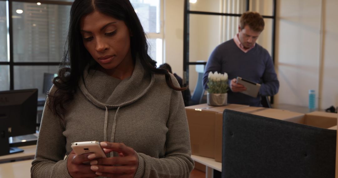 Woman Using Smartphone in Casual Office Setting with Busy Team