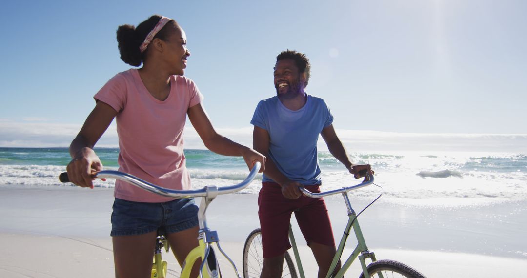 African american couple smiling and riding bikes on the beach - Free Images, Stock Photos and Pictures on Pikwizard.com