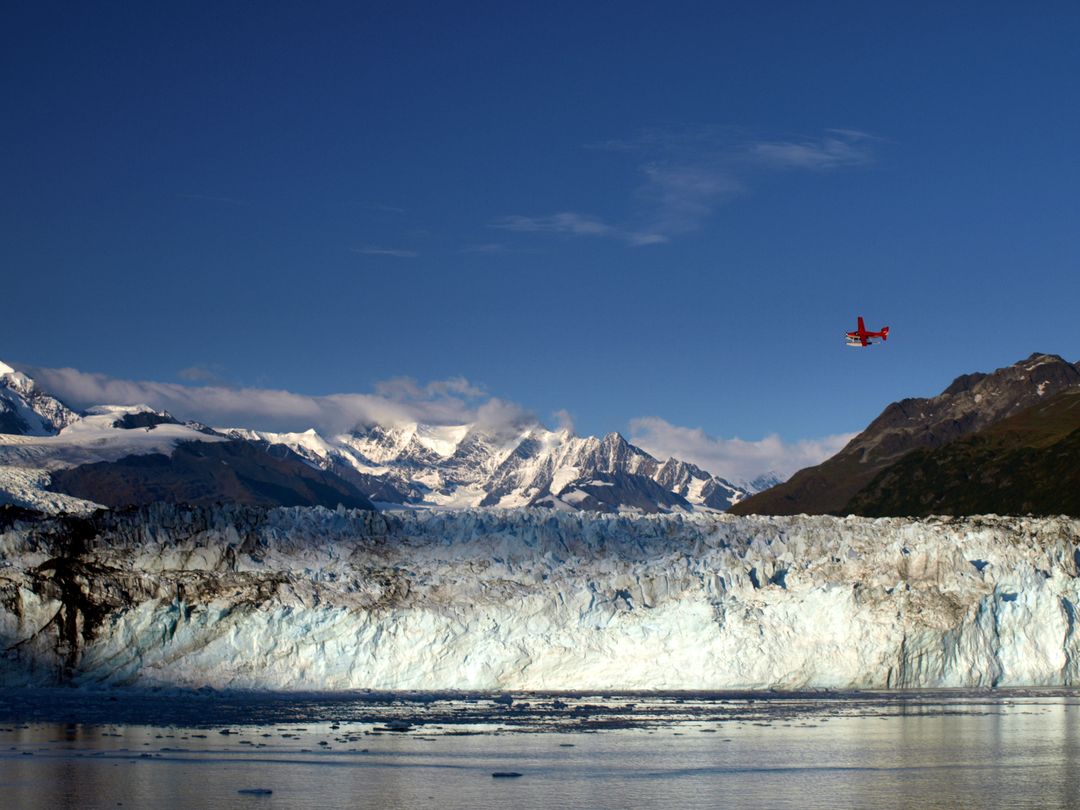 Red Seaplane Flying Over Massive Glacier and Snow-Capped Mountains