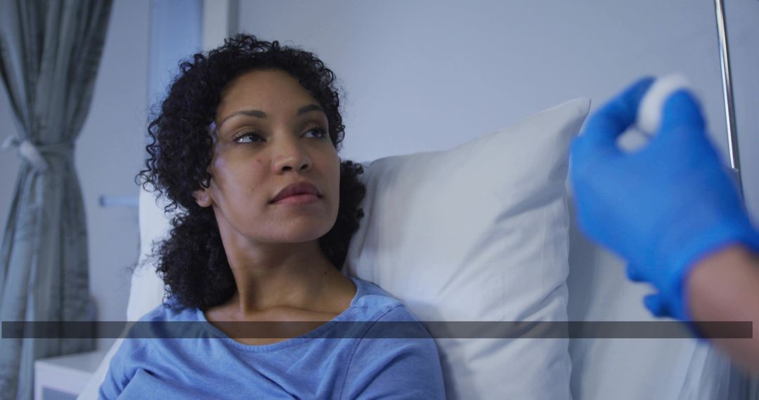 Patient receiving injection from gloved healthcare clinician while resting in hospital bed