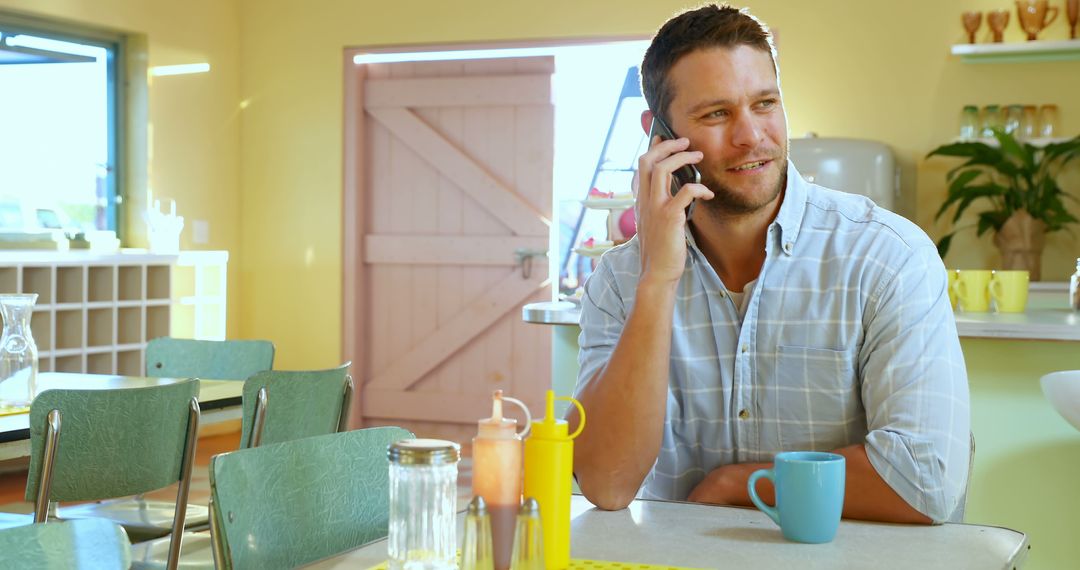 Smiling man having phone conversation at sunny cafe table - Free Images, Stock Photos and Pictures on Pikwizard.com