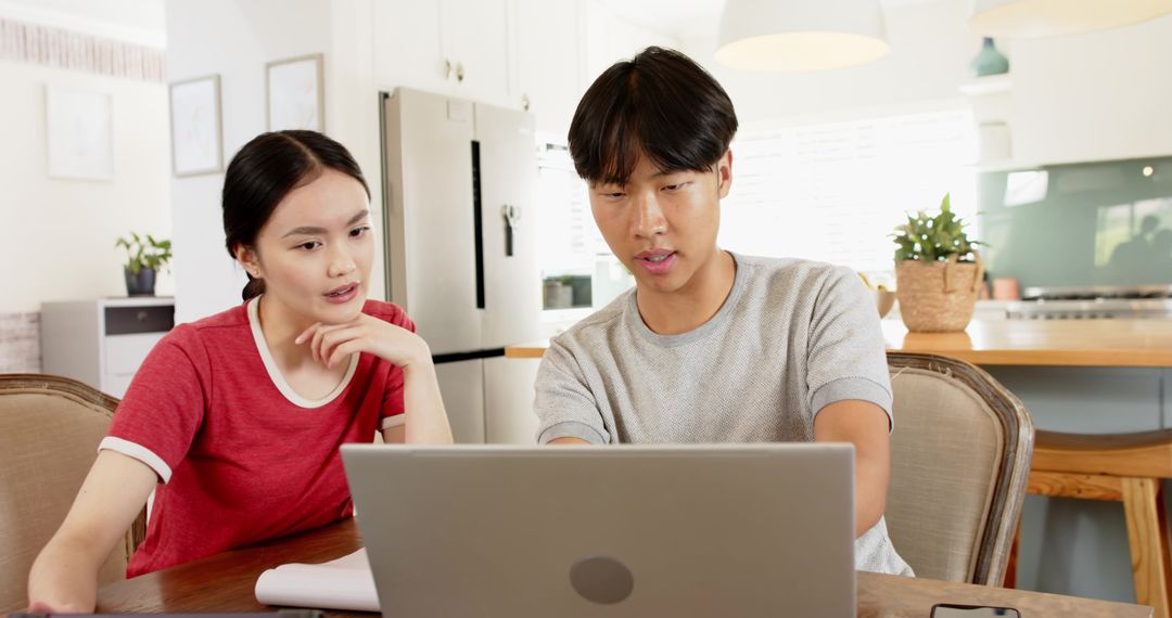 Asian Couple Collaborating at Home with Laptop and Notebook