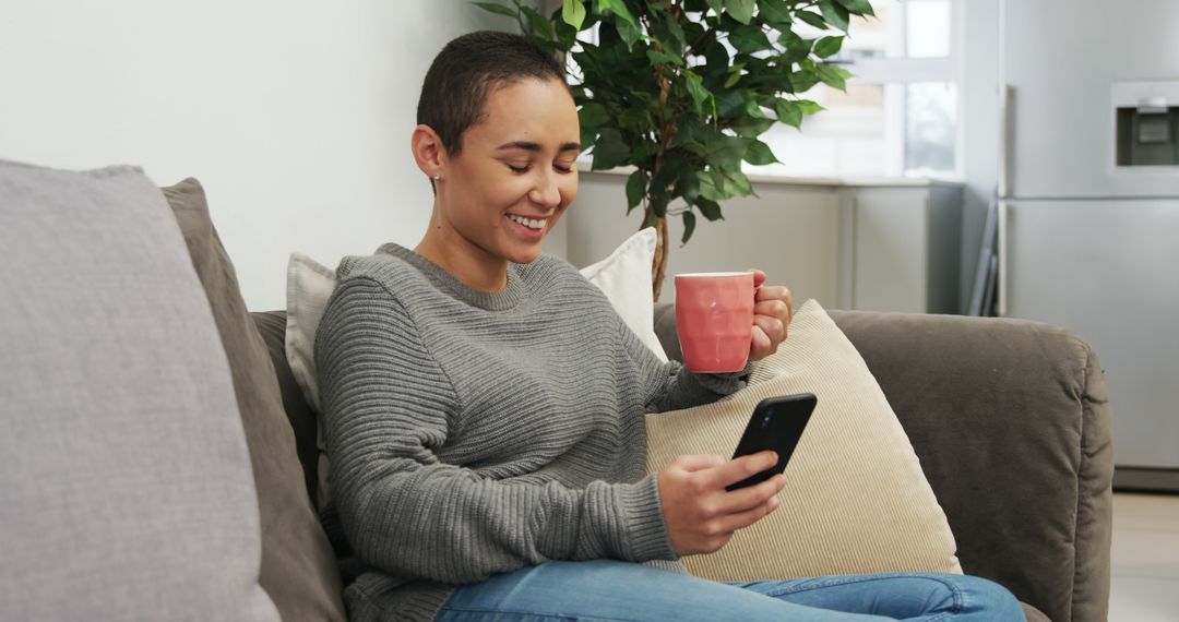 Smiling Woman Drinking Coffee And Using Smartphone On Couch - Free Images, Stock Photos and Pictures on Pikwizard.com