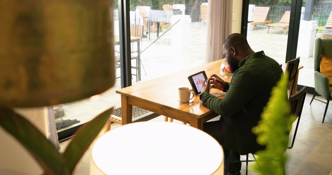 African American Man Analyzing Tablet Charts in Home Workspace with Coffee Mug