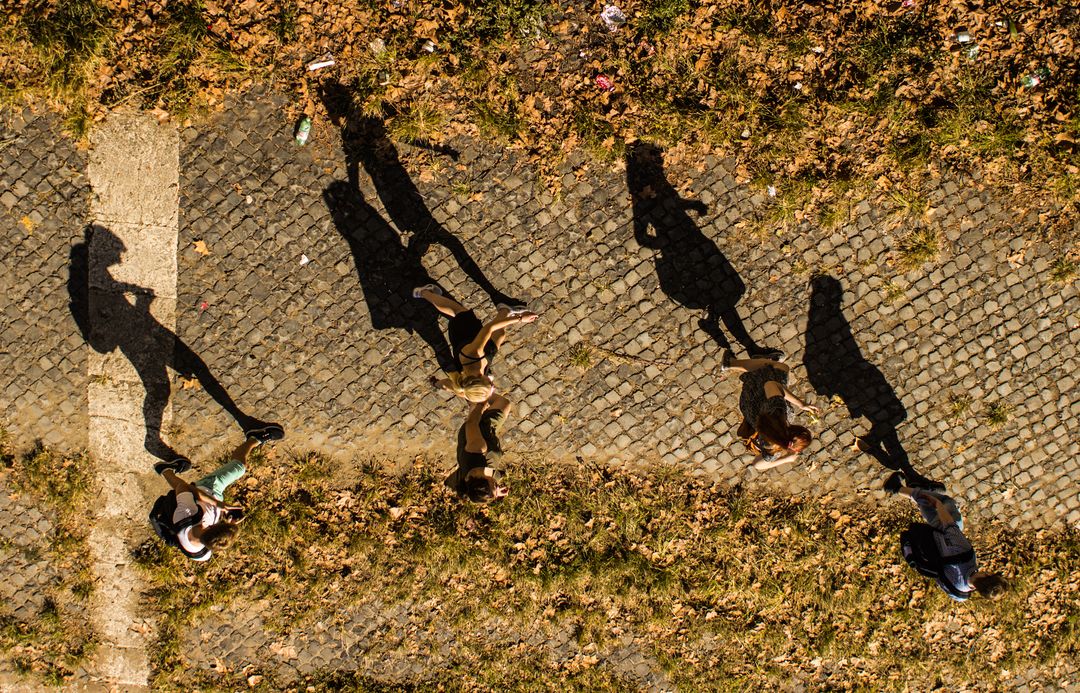 Group of People Casting Long Shadows While Walking on Cobbled Path - Free Images, Stock Photos and Pictures on Pikwizard.com