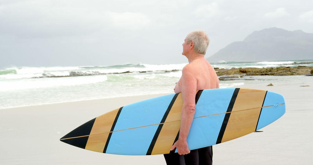 Senior Man Holding Surfboard on Beach Looking at Waves - Free Images, Stock Photos and Pictures on Pikwizard.com