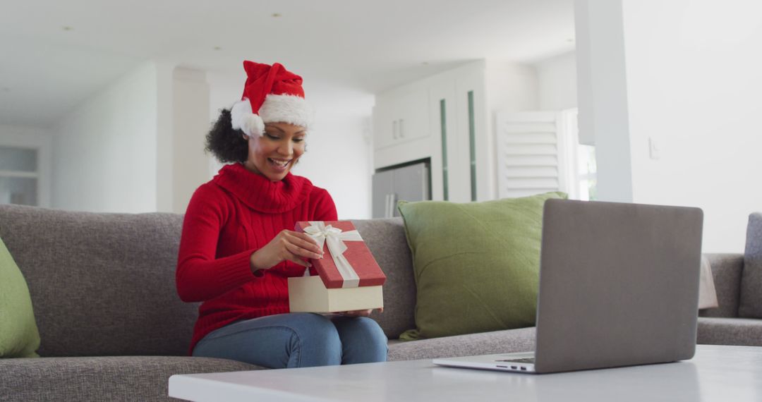 Woman Wearing Santa Hat Opening Holiday Gift During Video Call - Free Images, Stock Photos and Pictures on Pikwizard.com