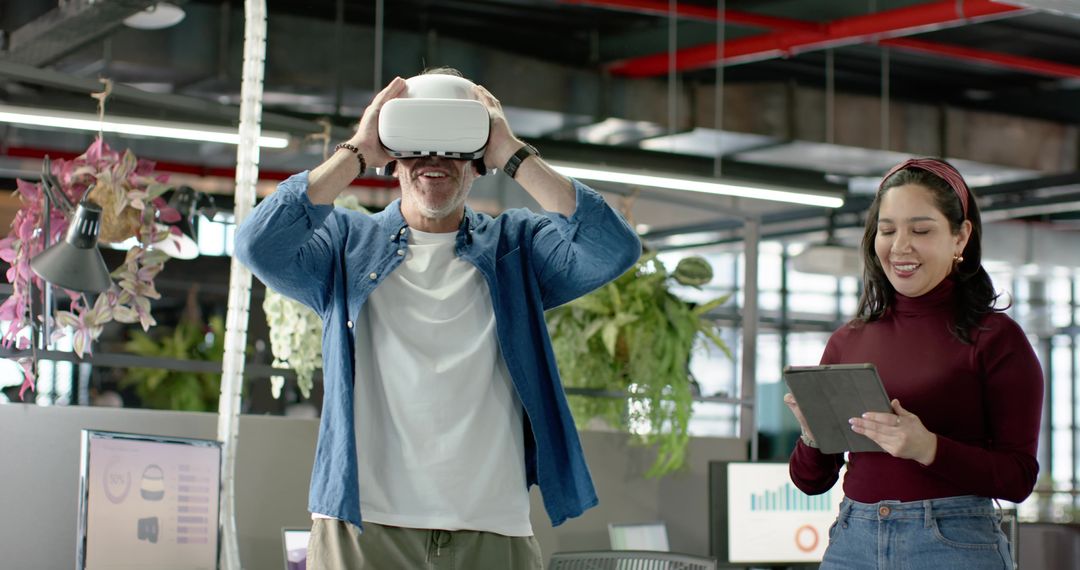 Mature man testing VR headset while coworker monitoring analytics on tablet in office