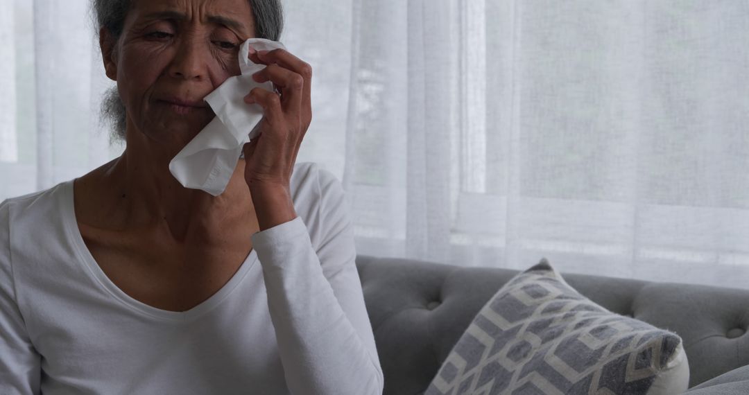 Senior Woman Crying Sitting on Gray Couch with Tissue - Free Images, Stock Photos and Pictures on Pikwizard.com