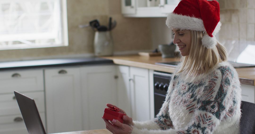 Woman Video Calling and Opening Christmas Gift in Festive Kitchen - Free Images, Stock Photos and Pictures on Pikwizard.com