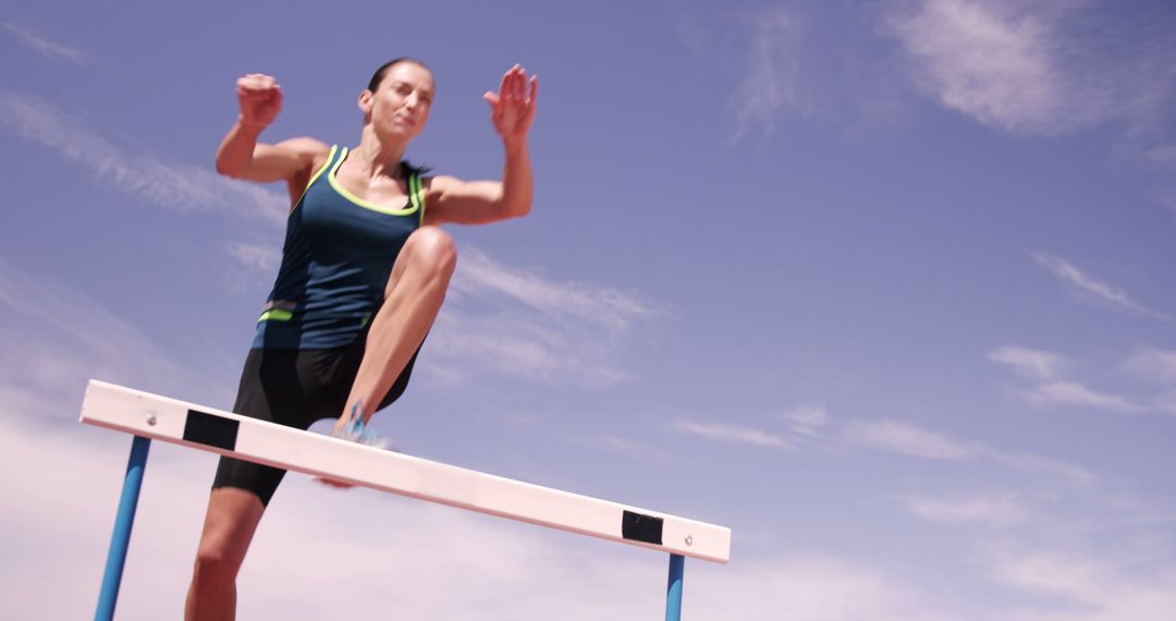 Female Athlete Clearing Hurdle on Outdoor Track - Free Images, Stock Photos and Pictures on Pikwizard.com