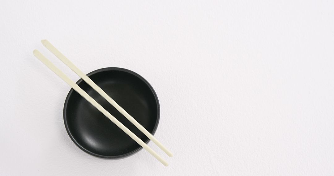 A pair of chopsticks rests on a black bowl against a white background, with copy space - Free Images, Stock Photos and Pictures on Pikwizard.com