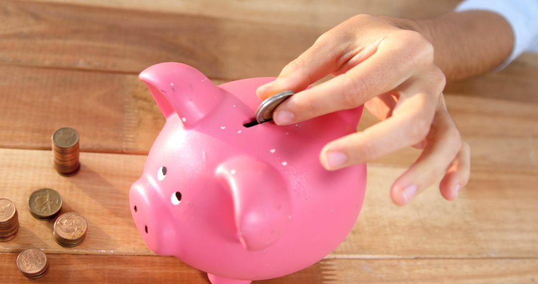 Hand Placing Coin into Pink Piggy Bank on Wooden Table - Free Images, Stock Photos and Pictures on Pikwizard.com