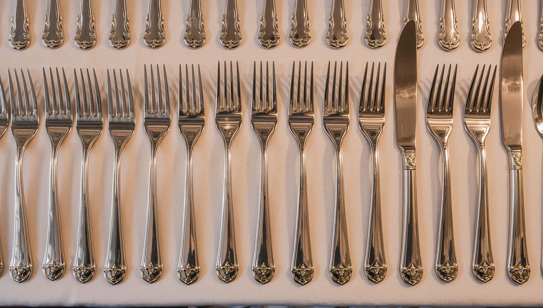 Displaying Polished Silver Flatware Lining Symmetrical Rows on White Linen Table