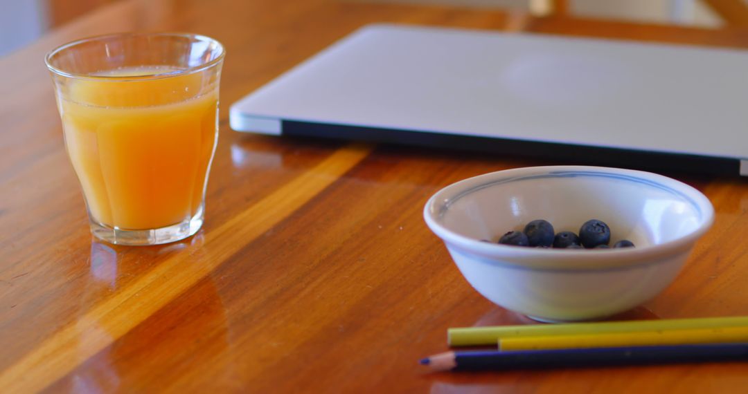 Bowl of Blueberries with Glass of Orange Juice and Laptop on Wooden Table - Free Images, Stock Photos and Pictures on Pikwizard.com