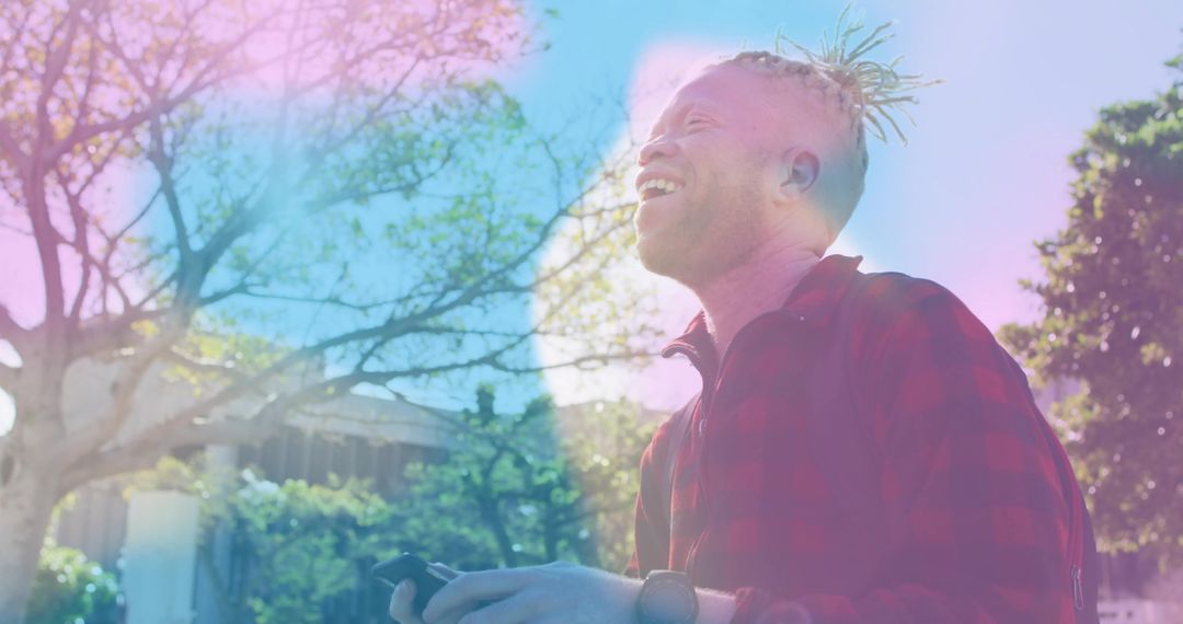 Smiling Young Man with Dreadlocks Using Smartphone in Sunlit Park
