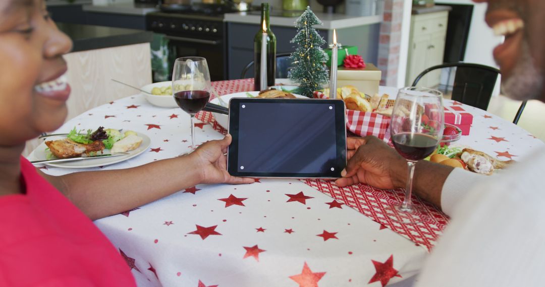 Couple Celebrating Christmas Dinner Holding Tablet at Festive Dinner Table - Free Images, Stock Photos and Pictures on Pikwizard.com