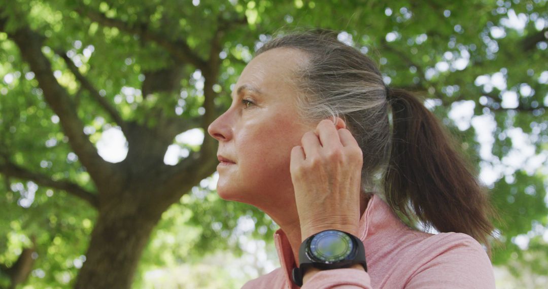 Mature Woman Adjusting Earbud Under Tree in Park - Free Images, Stock Photos and Pictures on Pikwizard.com