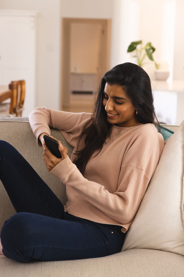 Asian Woman Relaxing on Sofa at Home Browsing Smartphone