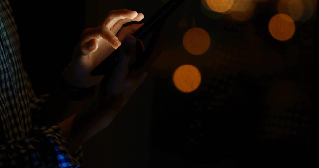 Man Using Smartphone in Dim Lighting with Amber Bokeh