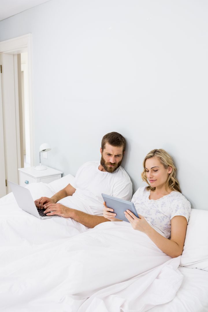 Couple using laptop and digital tablet in bed - Free Images, Stock Photos and Pictures on Pikwizard.com