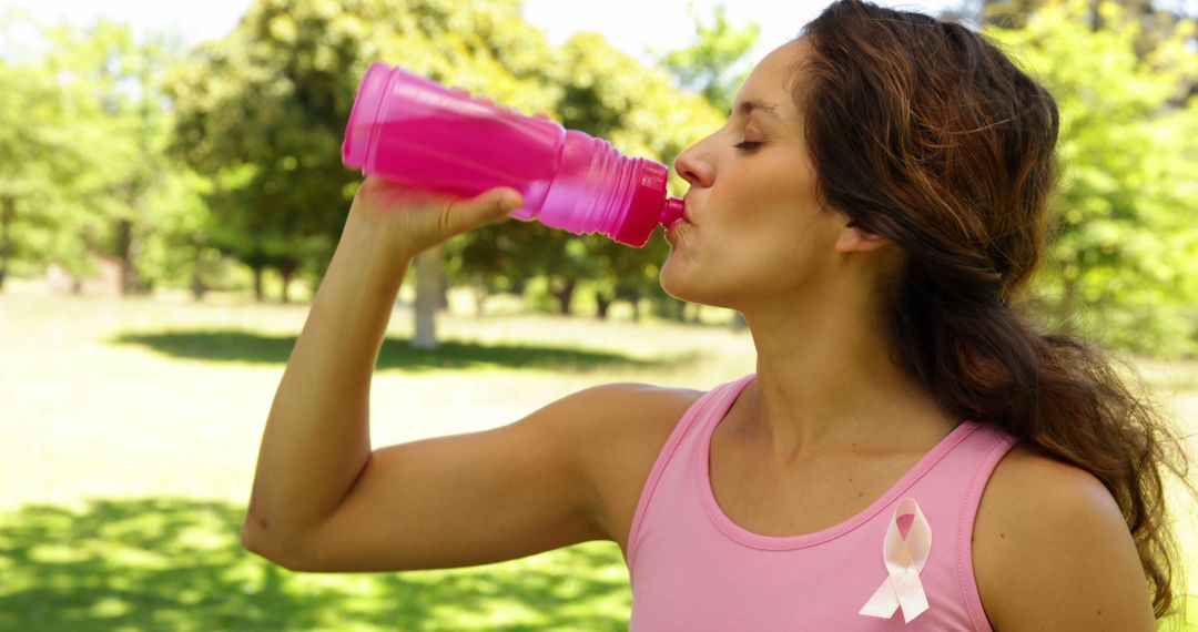 Woman Drinking Water in Park with Breast Cancer Awareness Ribbon - Free Images, Stock Photos and Pictures on Pikwizard.com