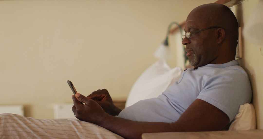Relaxed Senior Man with Smartphone Sitting on Bed Smiling