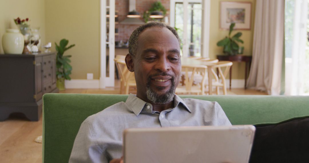 African American man smiling while using tablet in comfortable living room - Free Images, Stock Photos and Pictures on Pikwizard.com